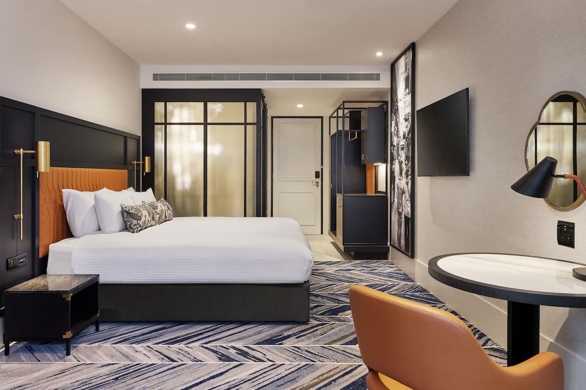 A hotel room with a bed, bedside table, chair, desk, and a large mirror.