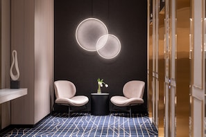 A modern lobby with two seating areas, a black circular table with a vase, and a geometric patterned floor.