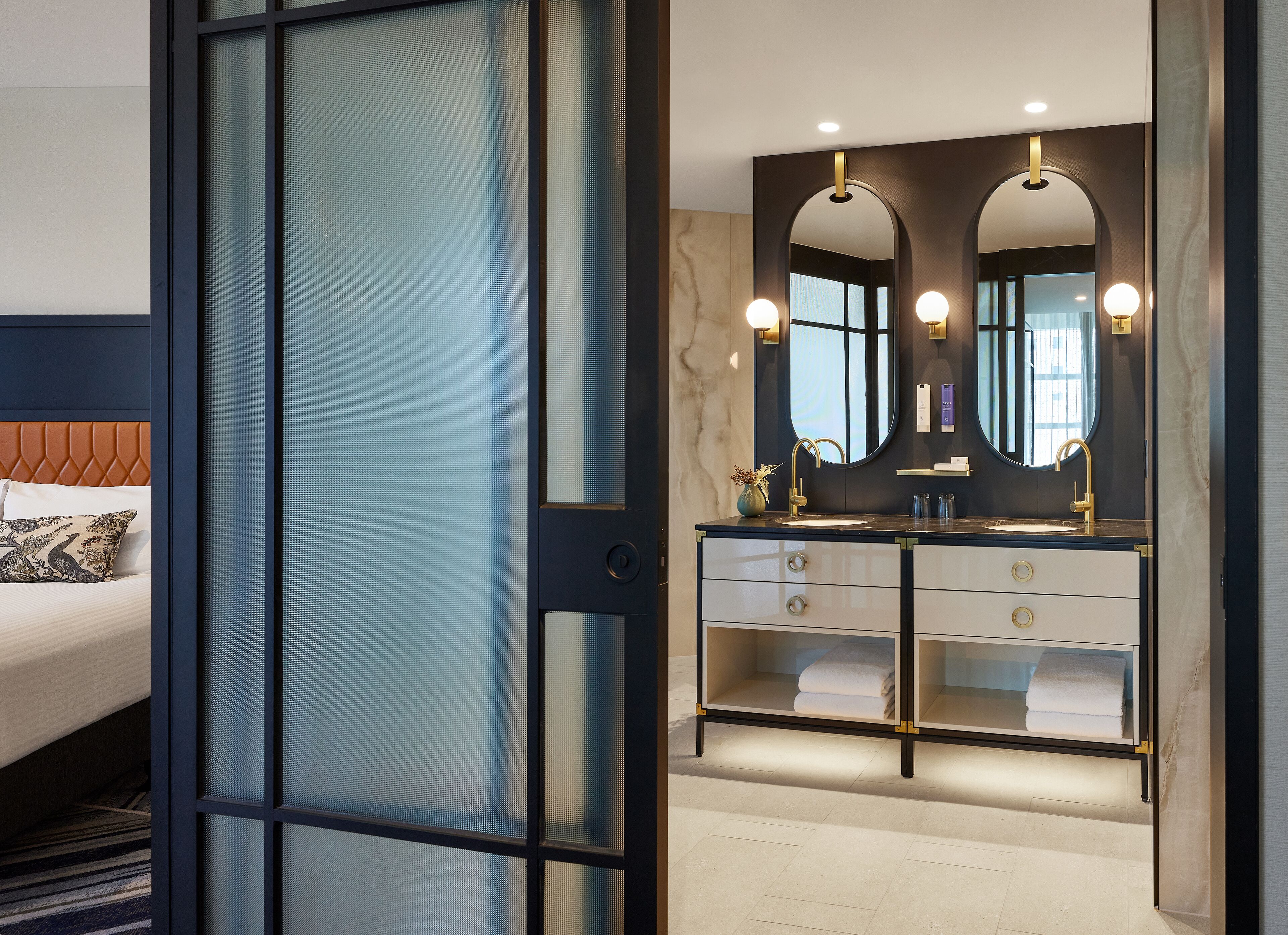 A modern hotel room with a bed, a large mirror, and a vanity with a sink.