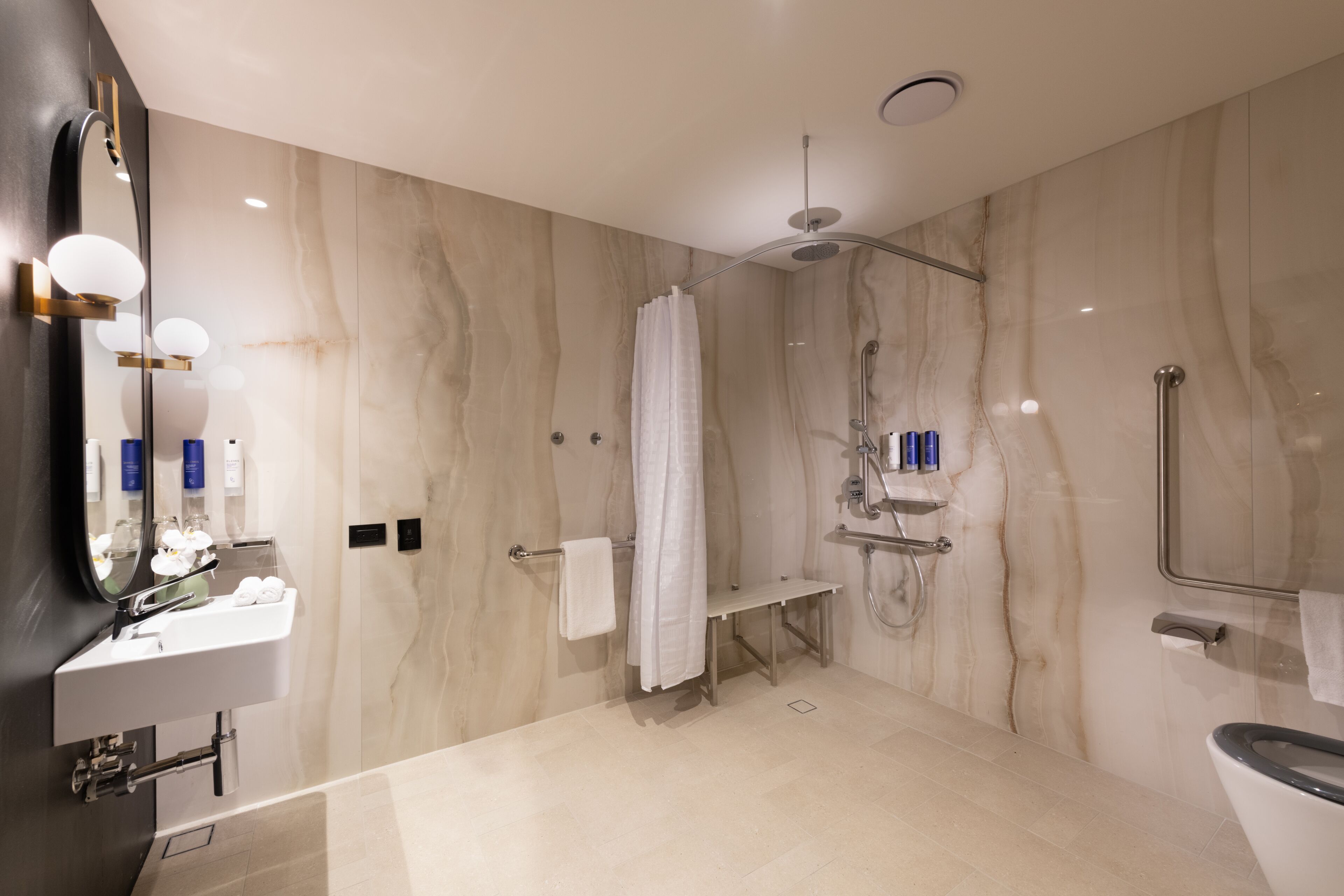 Un baño moderno con pared de mármol, un espejo grande, un lavabo, una ducha y un inodoro.