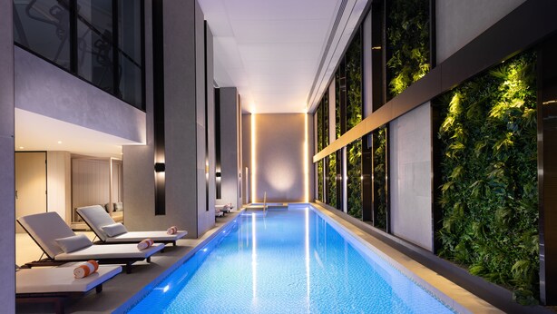Una piscina interior moderna con sillones de descanso y una pared verde.