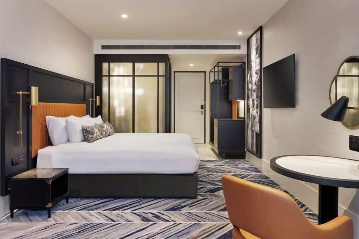 A hotel room with a bed, bedside table, chair, round table, and a large mirror.