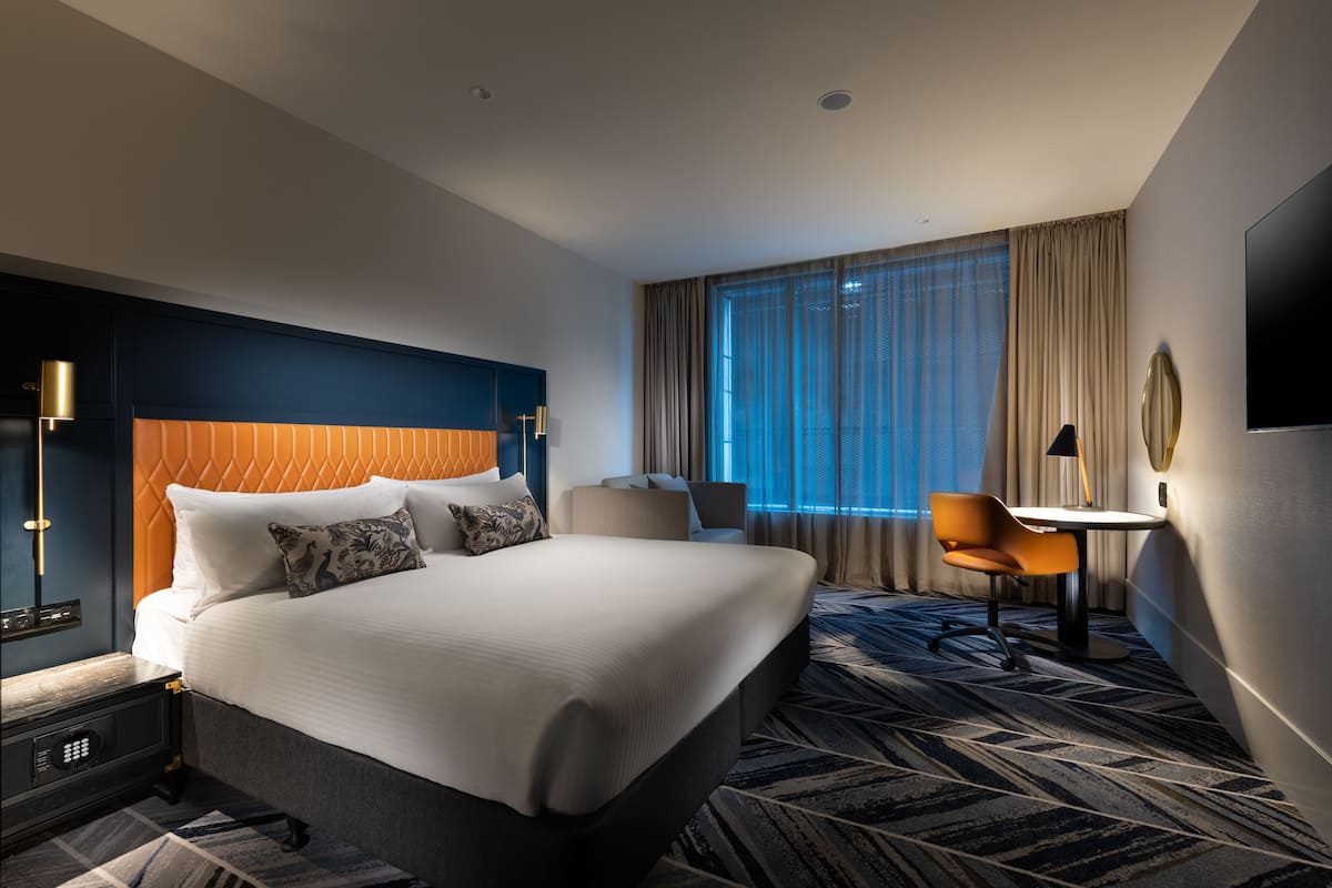 A hotel room with a large bed, a desk, a chair, and a TV.