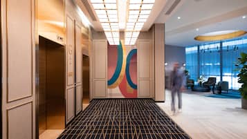 Rebedor modern d'hotel amb un paviment de disseny geomètric, una gran obra d'art abstracta a la paret i una zona de seients amb un finestral gran que ofereix vistes a l'exterior.