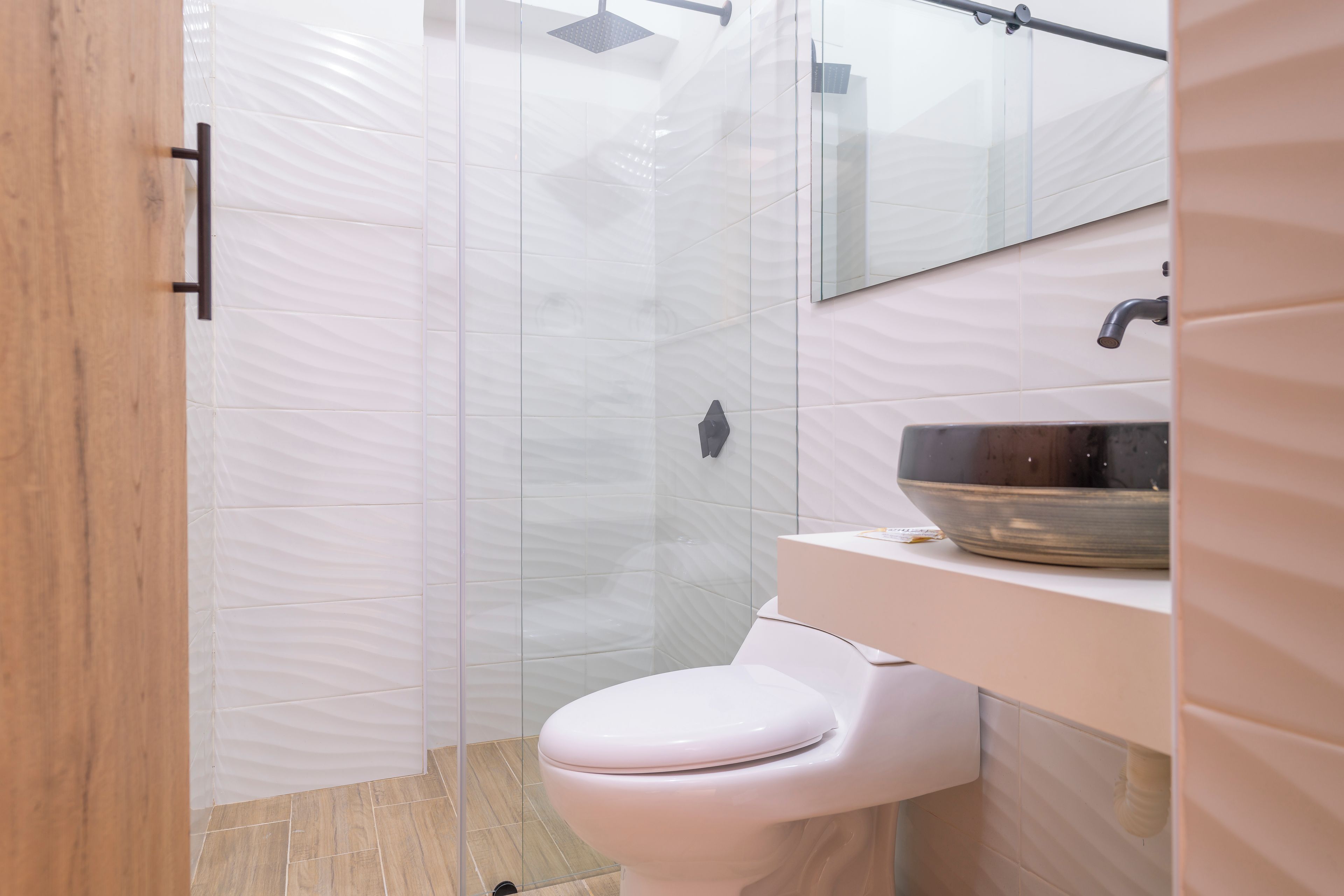 Une salle de bain moderne avec une douche à parois de verre, des toilettes blanches et un lavabo avec un receveur.