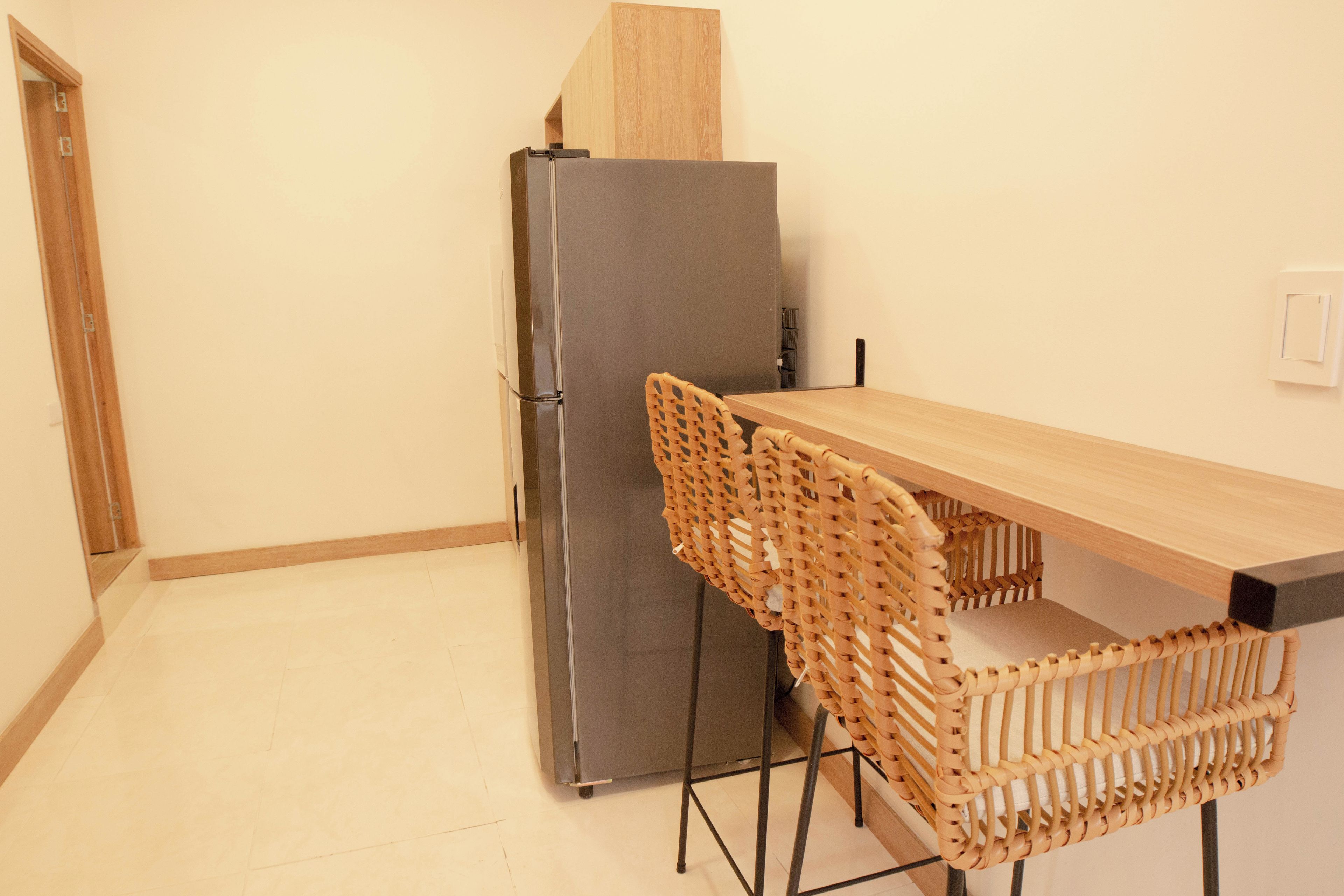 A compact kitchen with a stainless steel refrigerator, a wooden table, and a woven chair.