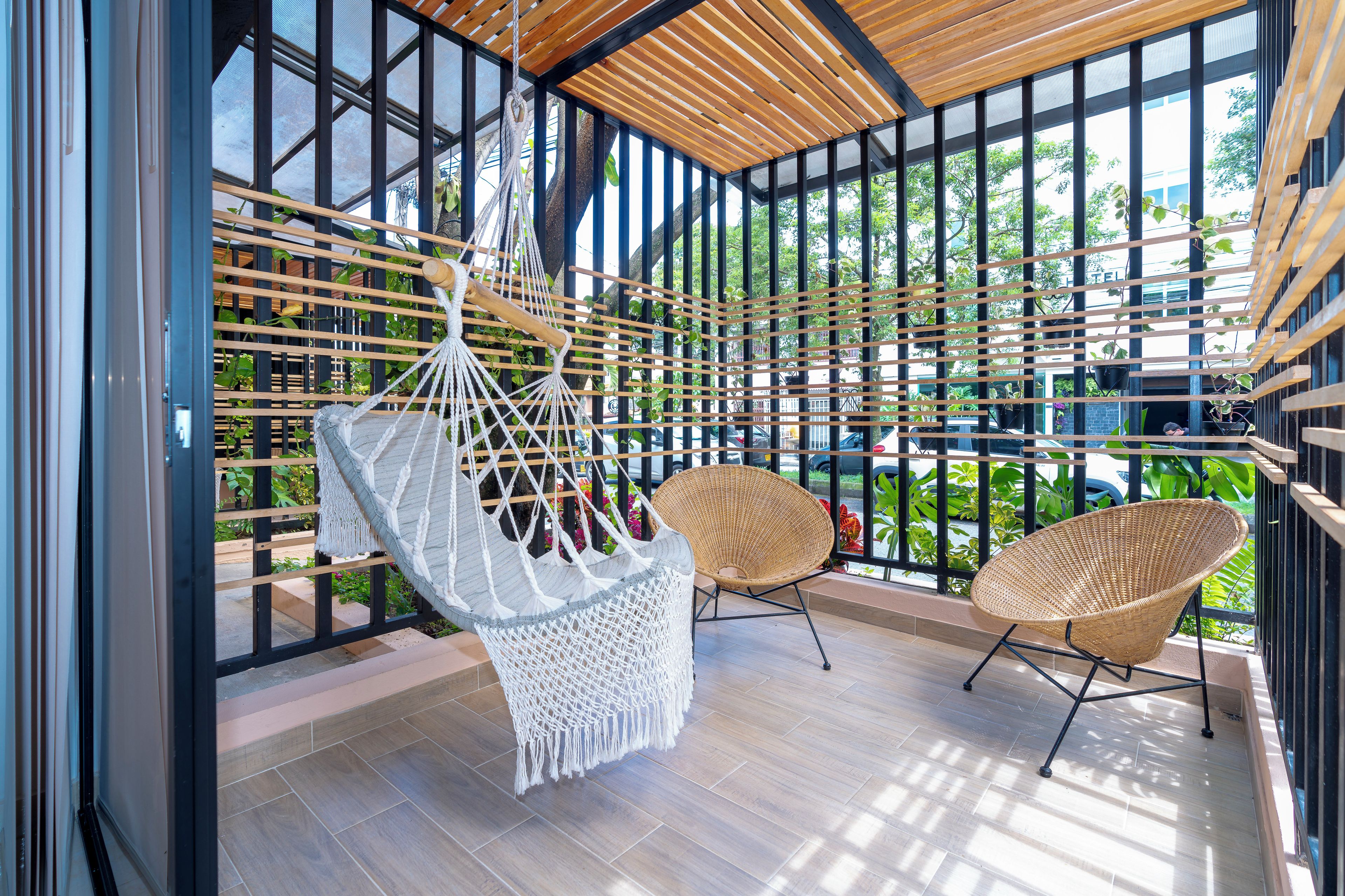 A covered outdoor seating area with a hammock, two wicker chairs, and a view of the street.