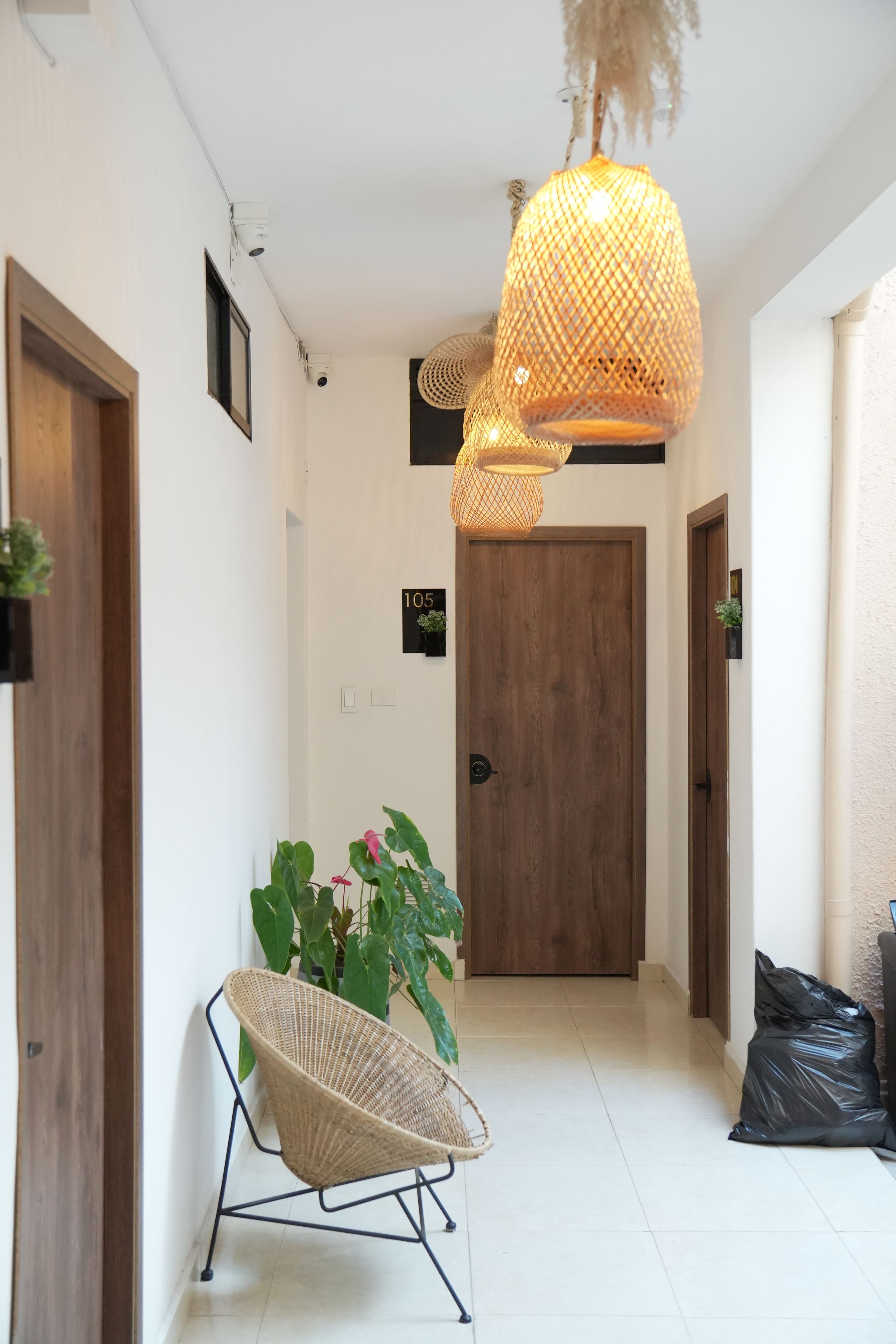 Un couloir avec un fauteuil en osier, une porte en bois et un luminaire suspendu.