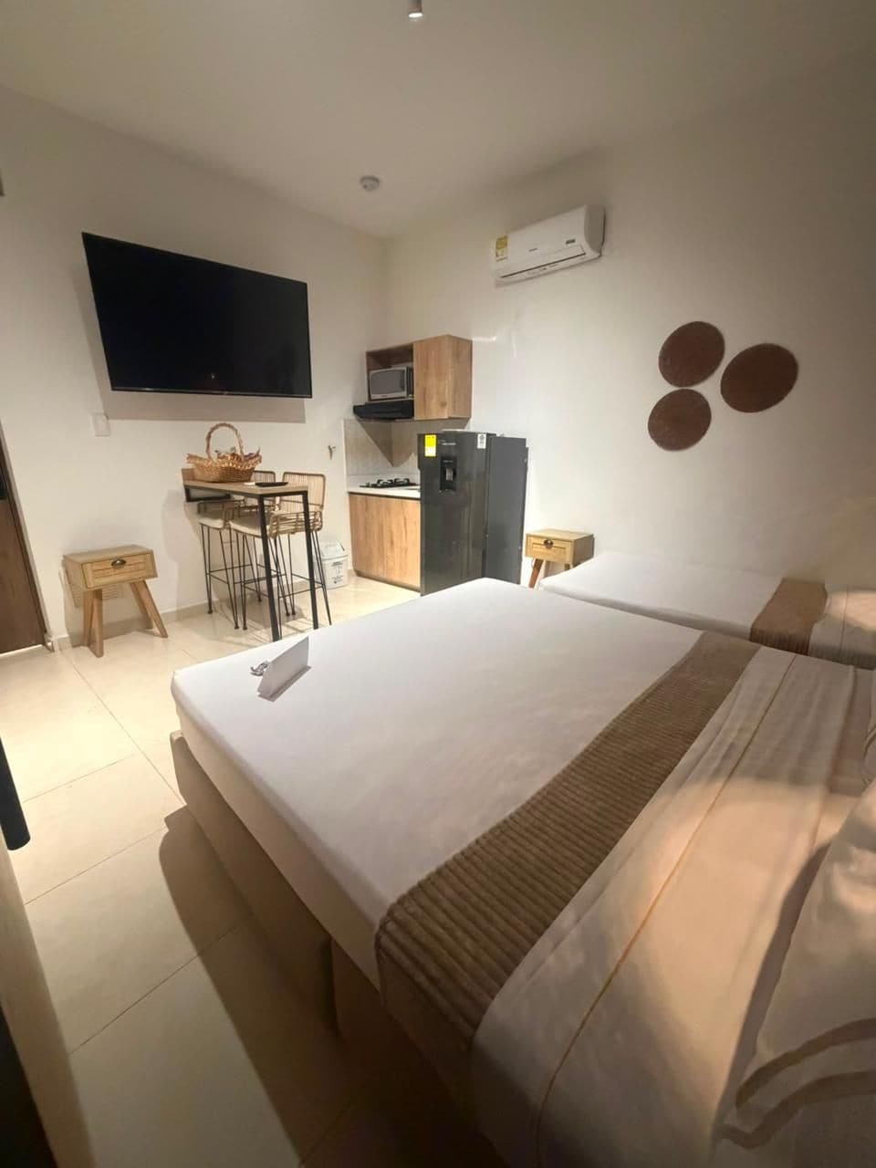 A hotel room with a bed, a desk with a chair, a television, and a kitchenette.