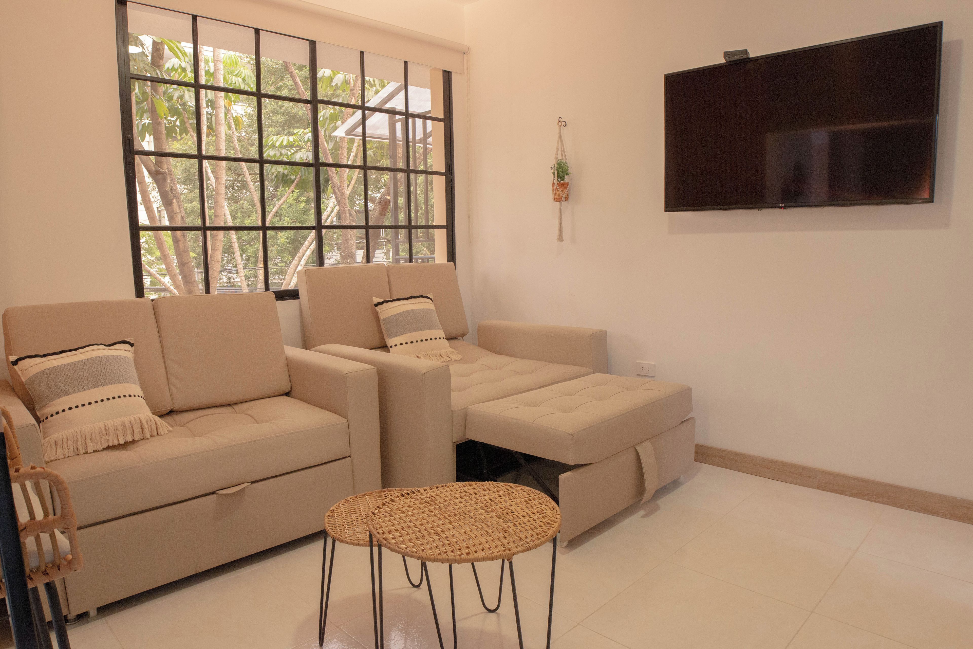 Un salon comprenant un canapé, une petite table ronde et un téléviseur fixé au mur.