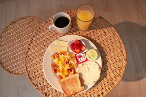 Une assiette de petit-déjeuner comprenant des œufs brouillés, du bacon, des toasts, des fraises et un verre de jus d’orange.
