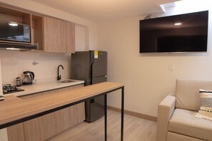 Une petite cuisine équipée d’un four à micro-ondes, d’une cuisinière, d’un évier et d’un réfrigérateur. Un téléviseur à écran plat est fixé au mur, au-dessus du comptoir.