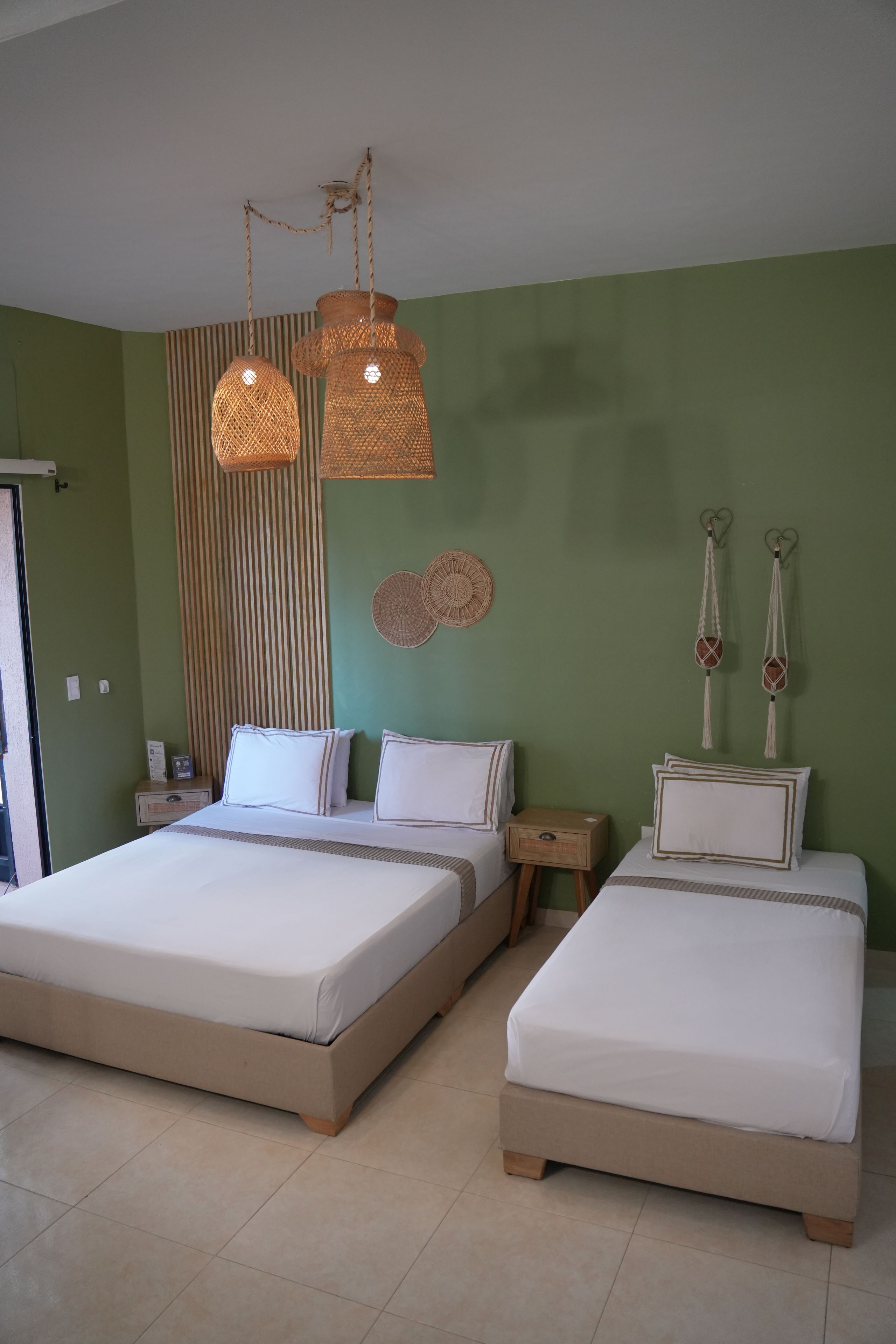 Una habitación con dos camas, una pared verde y una lámpara colgante.
