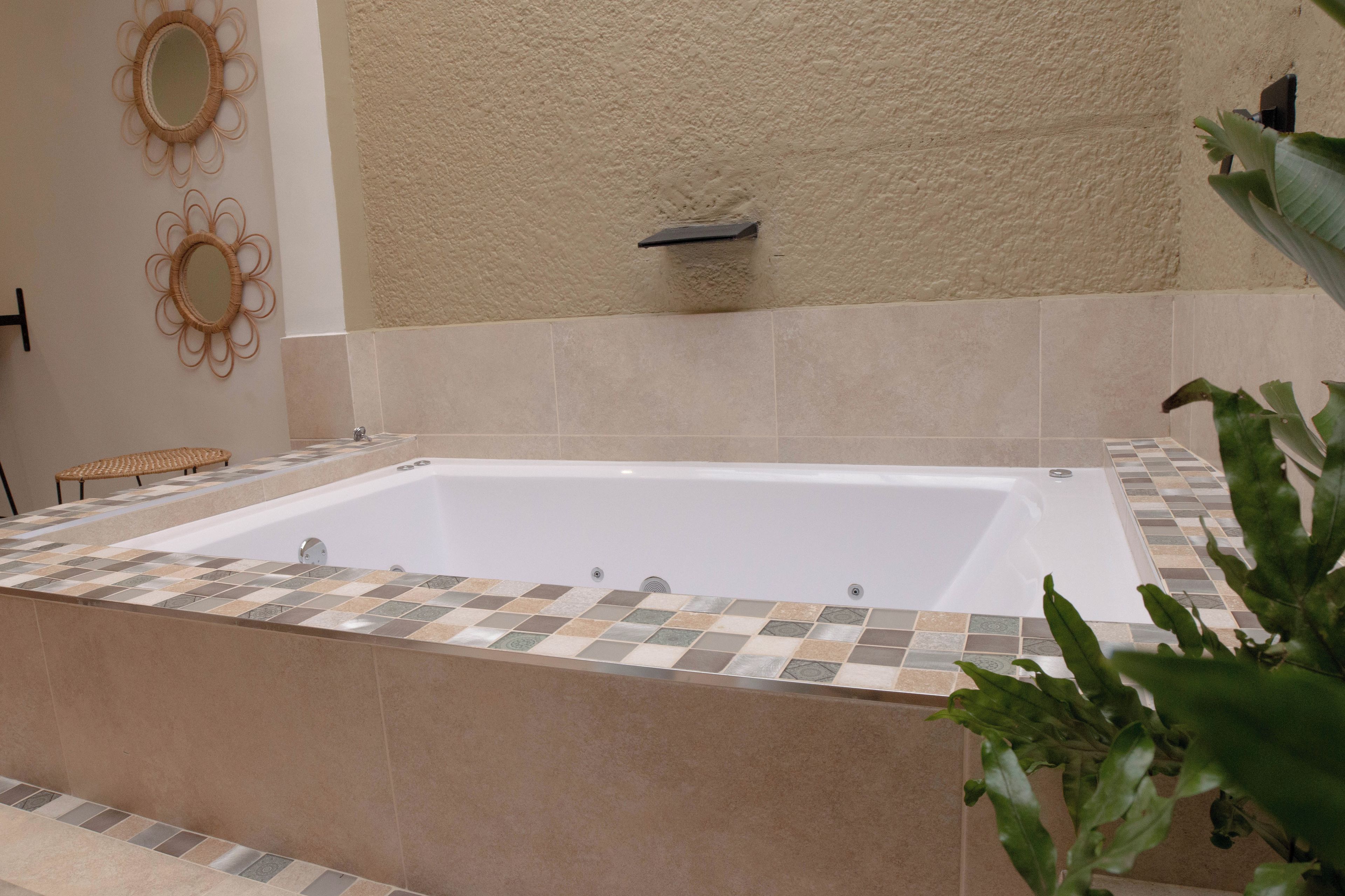 A bathroom with a large bathtub, tiled walls, and a small bench.