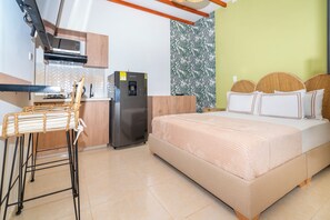 A compact hotel room with a kitchenette, a bed with a beige blanket, and a green accent wall. - Hotel La Casona Laureles Medellin (Medellín)