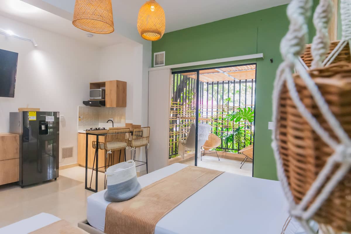 Ein modernes Schlafzimmer mit Bett, Nachttisch und Blick auf einen Balkon mit Pflanzen.
