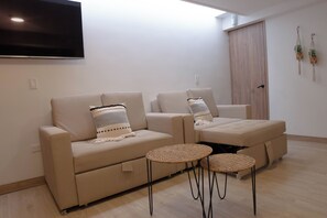 Un salon moderne comprenant un ensemble canapé, deux petites tables rondes et un téléviseur à écran plat fixé au mur.