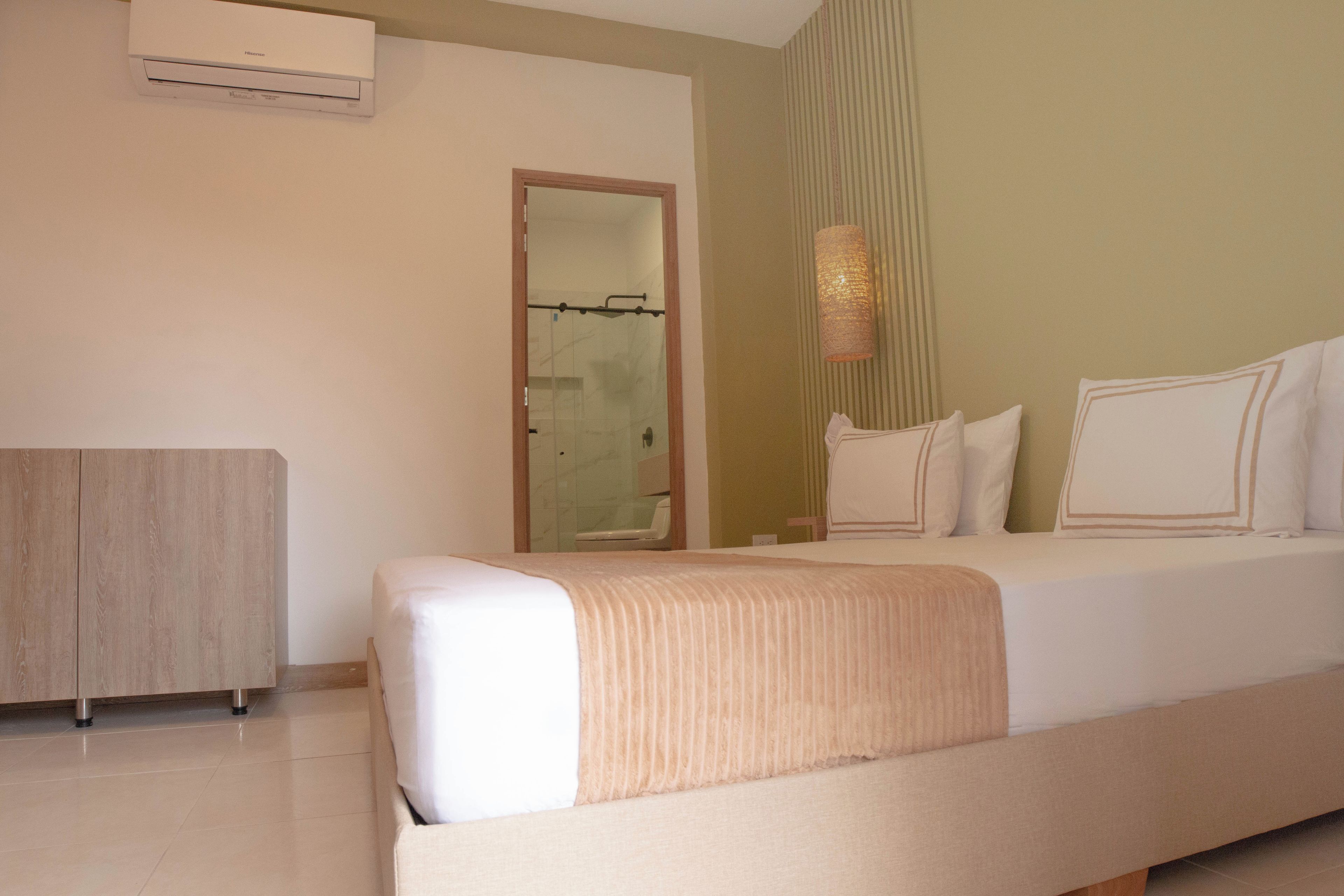 A hotel room with a bed, a bedside table, a wardrobe, and an air conditioning unit.