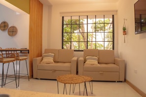 A living room with two sofas, a small round table, and a window with a view of trees. - Hotel La Casona Laureles Medellin (Medellín)