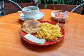 Une assiette avec des œufs brouillés, une tranche de pain grillé et du beurre, le tout sur une assiette rouge.