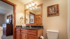Une salle de bain avec un meuble-lavabo en bois, un évier, des toilettes et un grand miroir avec éclairage intégré.