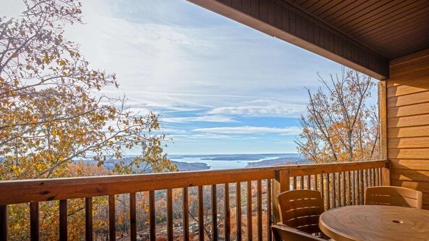 Une terrasse en bois avec une table et des chaises, offrant une vue panoramique sur des arbres et une étendue d’eau.
