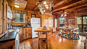 A wooden cabin interior with a kitchen, dining area, and a large window. - Cabin in a gated resort with HOT TUB, RESORT POOL, BBQ GRILL, WOOD FIREPLACE  (Pigeon Forge)