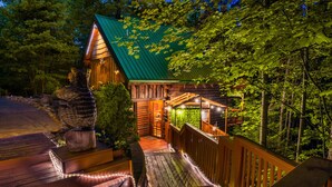 A wooden cabin with a green roof, surrounded by trees. - Cabin in a gated resort with HOT TUB, RESORT POOL, BBQ GRILL, WOOD FIREPLACE  (Pigeon Forge)