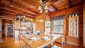 A wooden cabin interior with a dining table set for four, a ceiling fan, and a kitchen area with a microwave and cabinets. - Cabin in a gated resort with HOT TUB, RESORT POOL, BBQ GRILL, WOOD FIREPLACE  (Pigeon Forge)