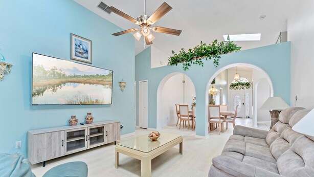 A spacious living room with a large flat-screen TV, a ceiling fan, and a dining area with a table and chairs.
