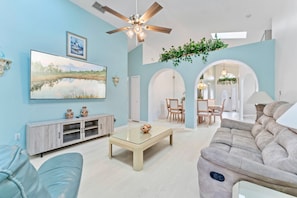 A spacious living room with a large flat-screen TV, a ceiling fan, and a dining area with a table and chairs. - Family, Pool View, Pickleball, Themed Villa Minutes from Disney! Massage Chair~ (Kissimmee)