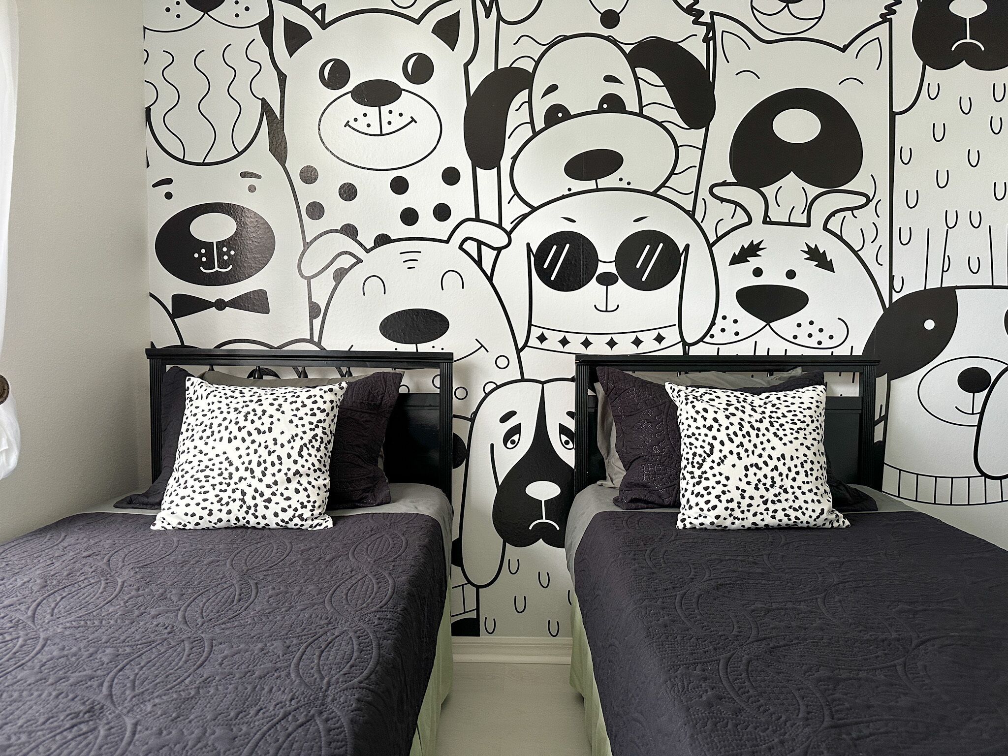 A bedroom with two beds, each with a patterned pillow and a wall mural of stylized animal faces.