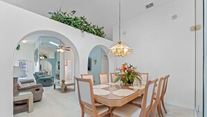 A dining area with a round table, six chairs, and a hanging light fixture.