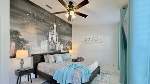 A bedroom with a bed, a ceiling fan, a nightstand, a lamp, a wall with a castle mural, and a motivational quote.