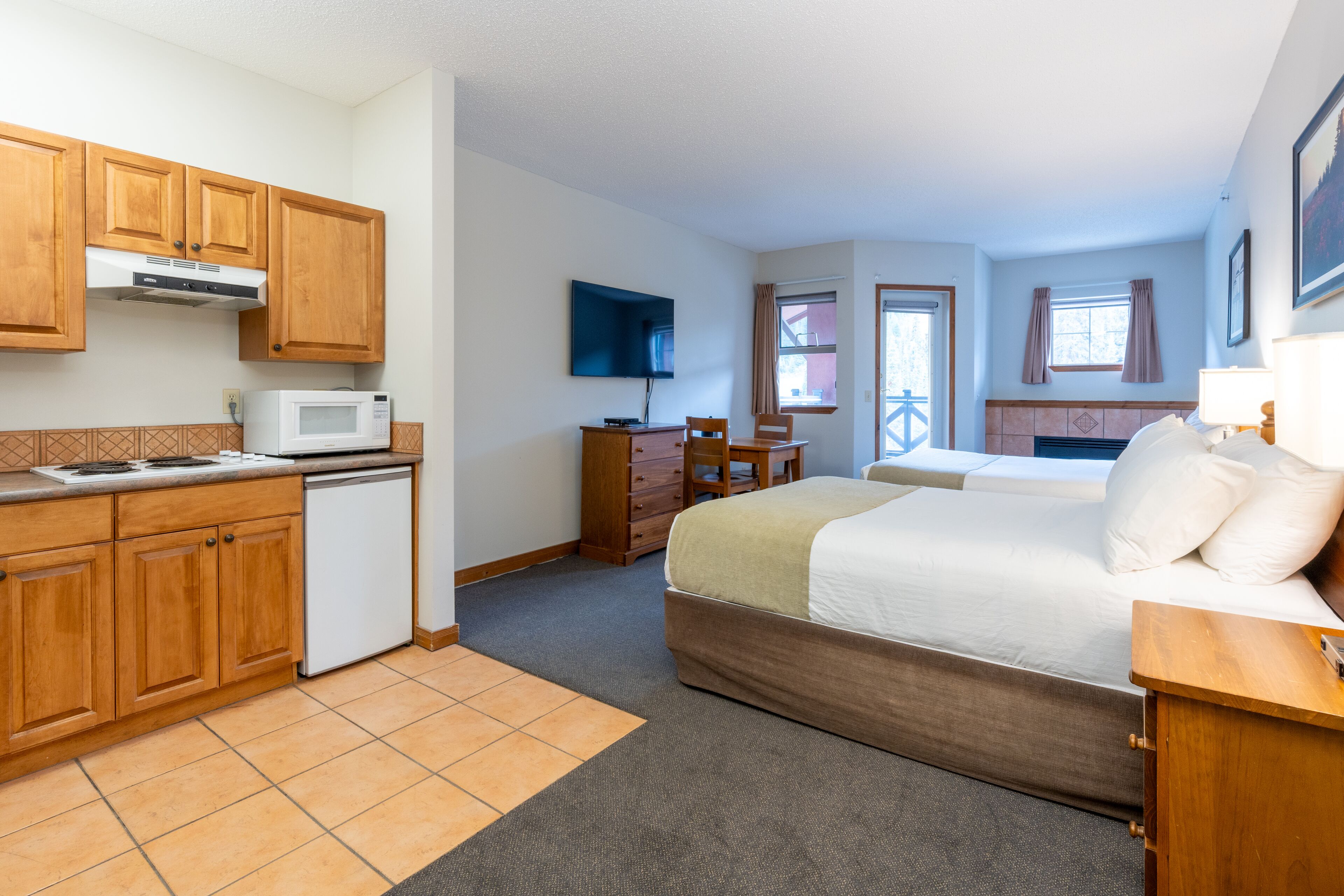 Una habitación de hotel compacta con kitchenette, cama, escritorio y televisor.