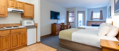 Una habitación de hotel compacta con kitchenette, cama, escritorio y televisor.
