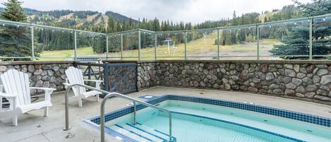 A pool area with a stone wall, white chairs, and a view of mountains.