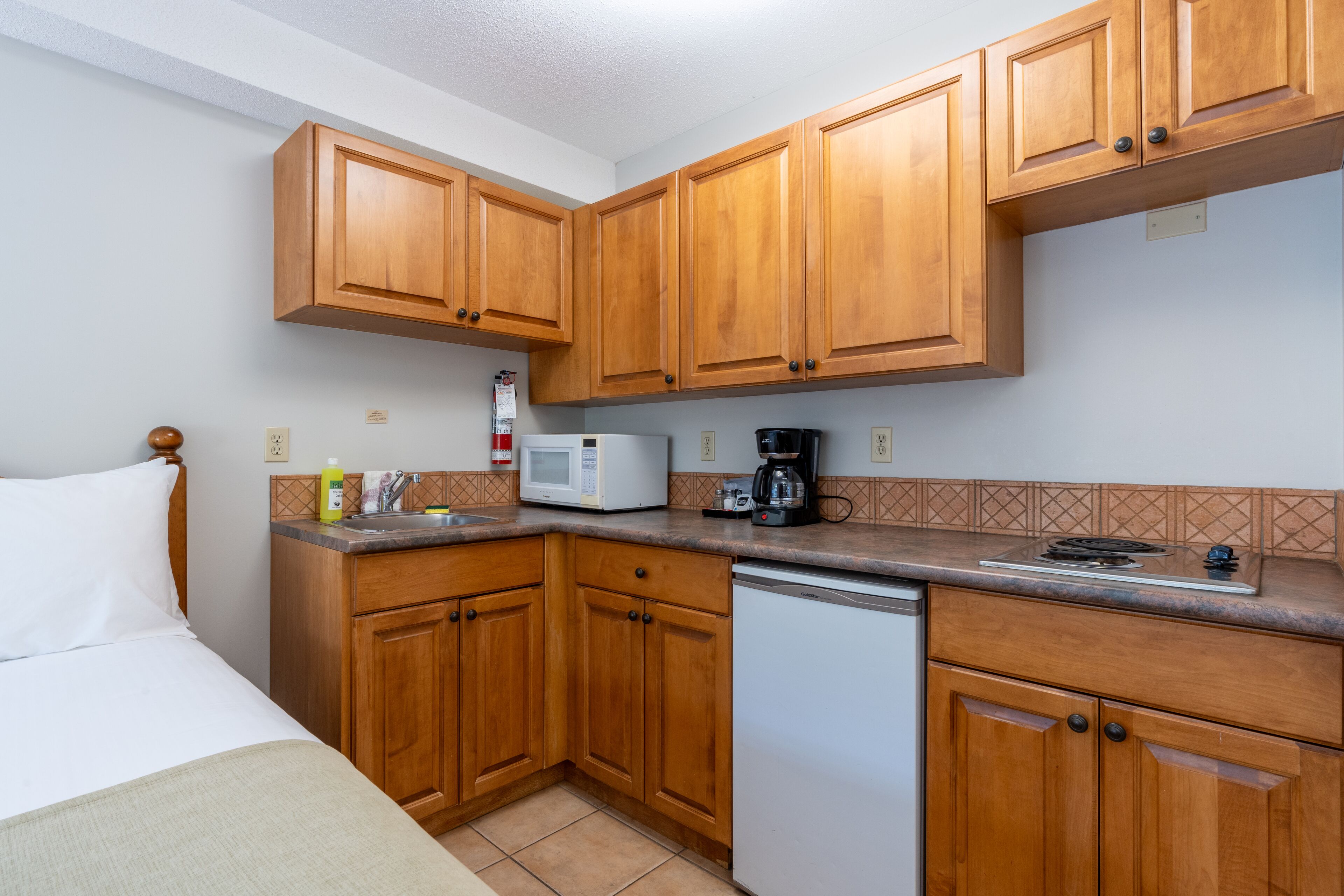 A compact kitchen with wooden cabinets, a microwave, a coffee maker, and a dishwasher.