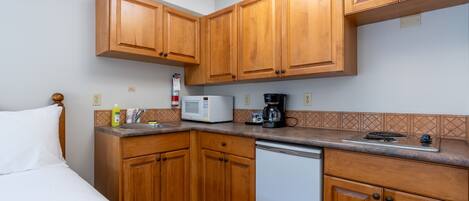 A compact kitchen with wooden cabinets, a microwave, a coffee maker, and a dishwasher.