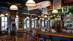 Un espace bar avec des tables et des chaises en bois, un comptoir avec des tabourets, ainsi que divers panneaux et éléments de décoration.