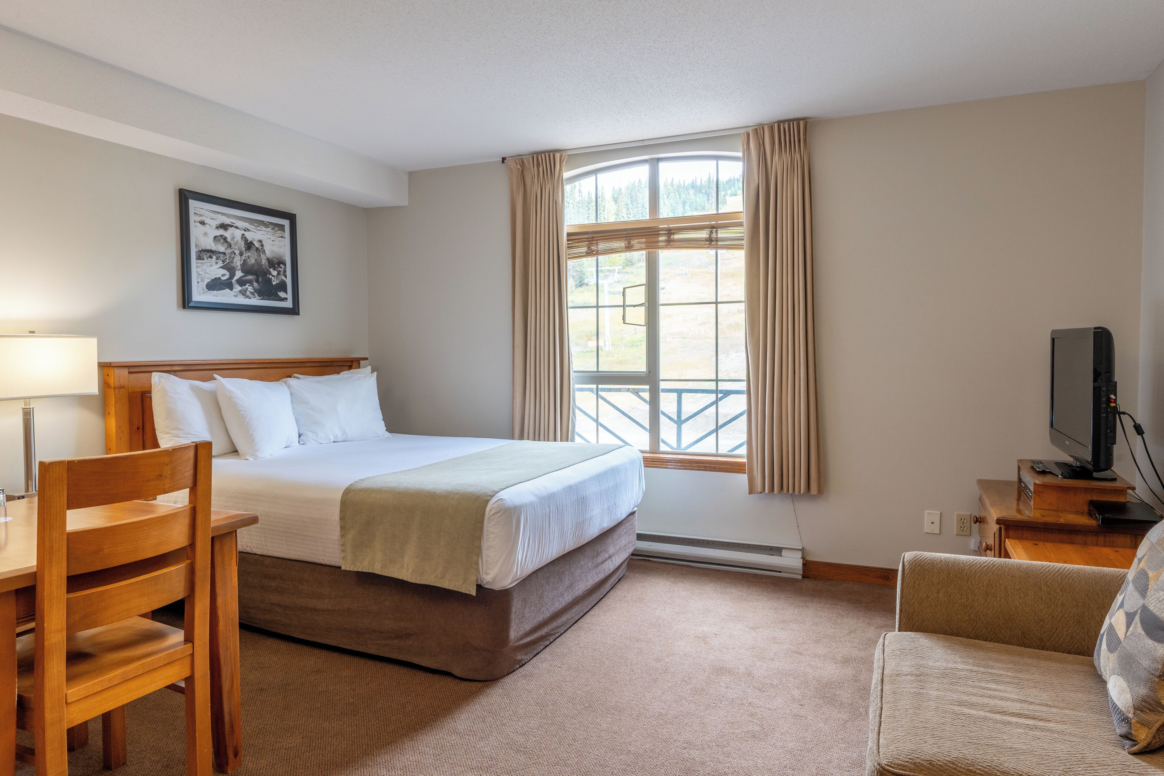 A hotel room with a bed, a desk, a chair, a television, and a window with curtains.