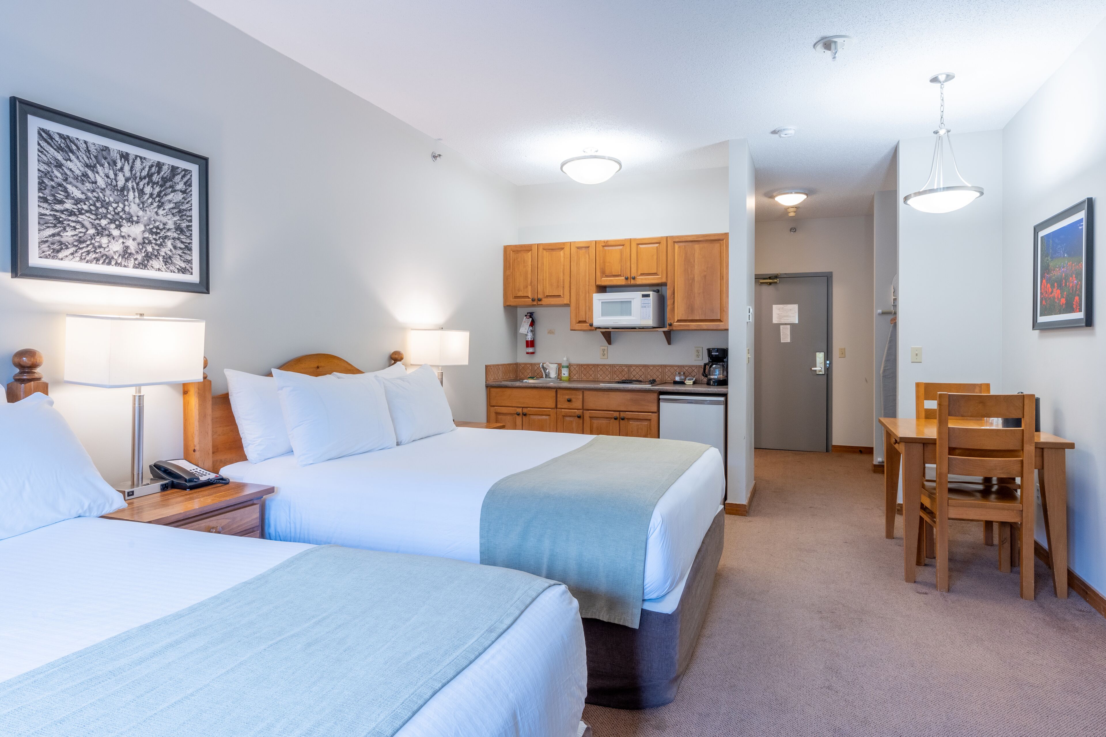 A hotel room with two beds, a kitchenette, and a dining area.