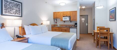 A hotel room with two beds, a kitchenette, and a dining area.
