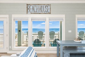 A beach house with a sign reading 'BEACHHOUSE' above a set of glass doors. Inside, there is a table with chairs and a view of the ocean. - Pet Friendly Beachfront Getaway Dream with Hot Tub & Fire Pit (Crystal Beach)