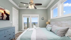 Une chambre à coucher avec un lit, un ventilateur de plafond, une grande fenêtre et une vue sur l’océan.