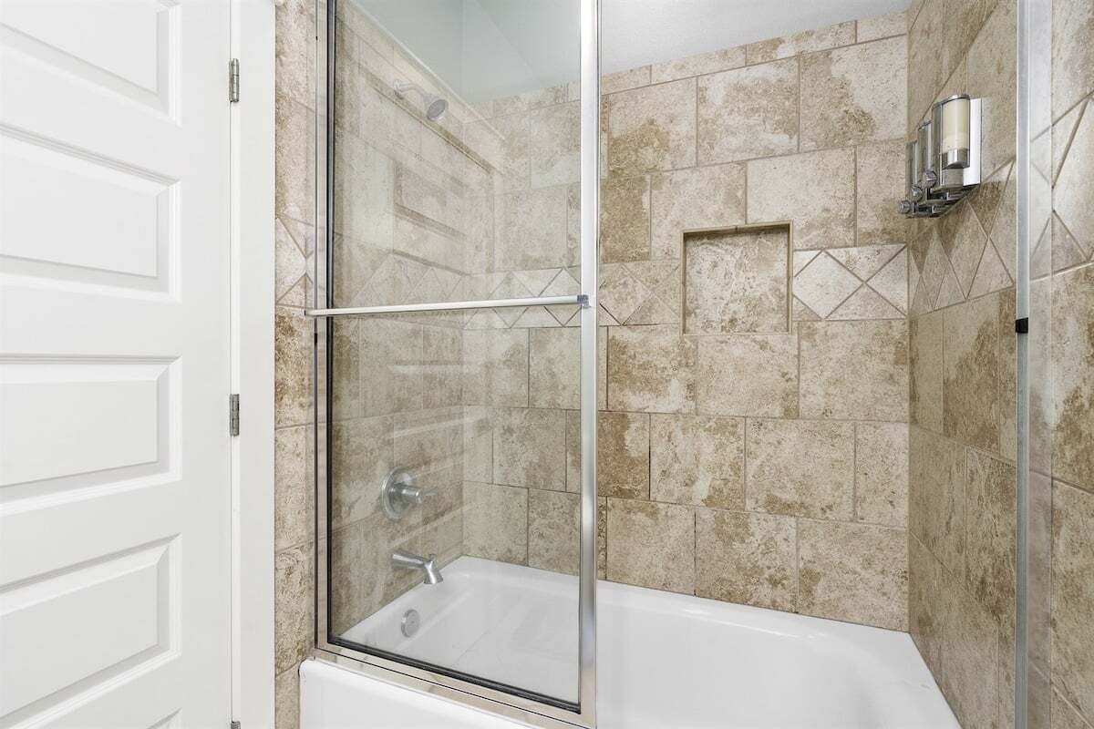 A modern bathroom with a glass-enclosed shower, a white bathtub, and beige tiled walls.