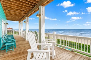 A wooden deck with white and turquoise Adirondack chairs, a wooden ceiling, and a view of the ocean.