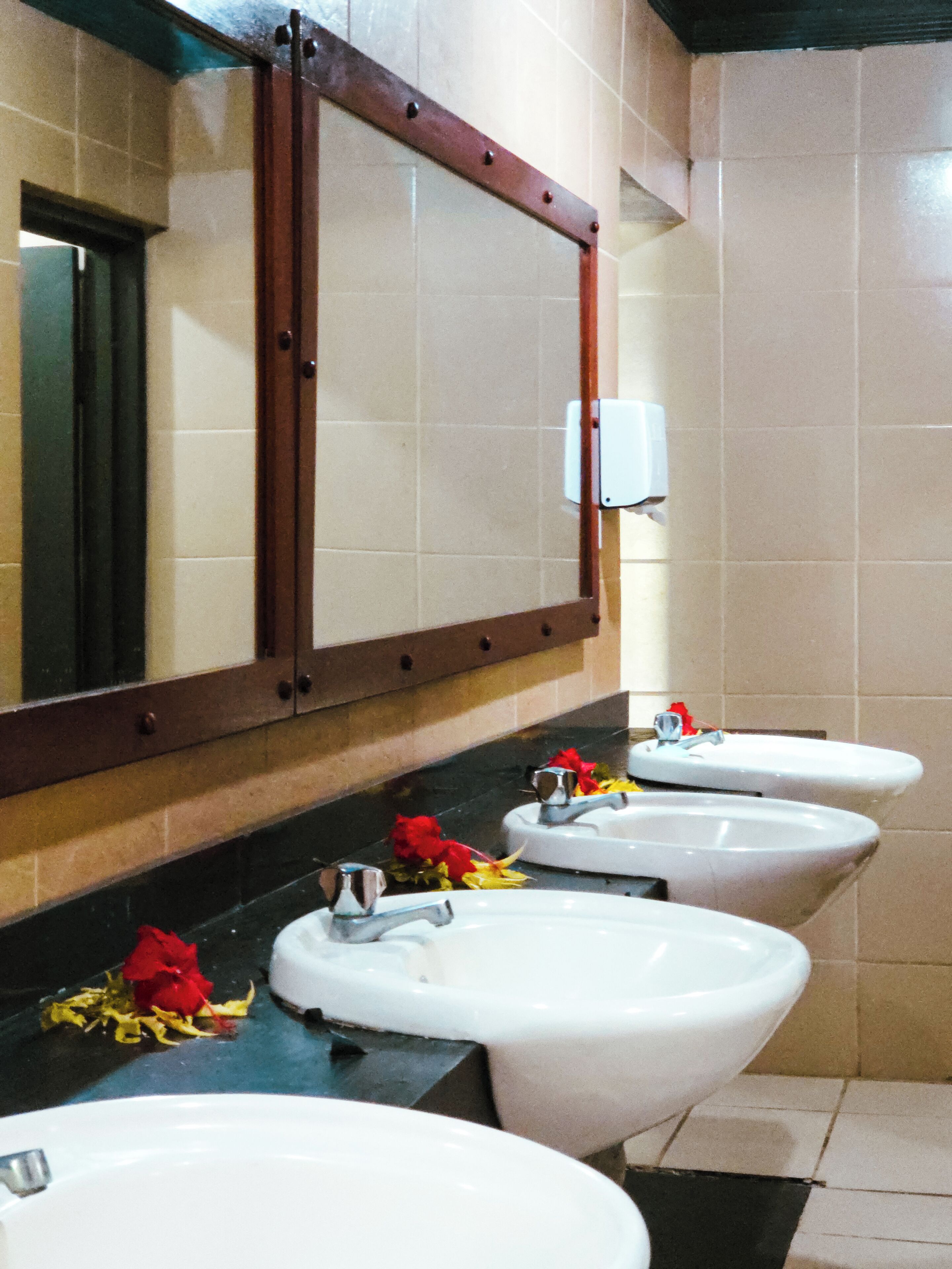 A public restroom with three sinks, a mirror, and a hand dryer.