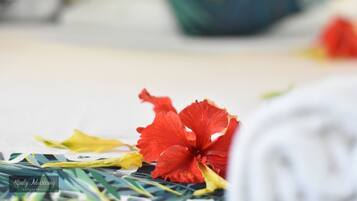 A close-up of a red hibiscus flower and some green leaves on a surface, with a blurred background.