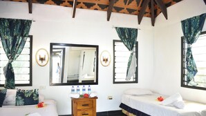 A room with two beds, a wooden nightstand with water bottles, a mirror, and tropical-themed curtains. - Coralview Island Resort (Tavewa Island)